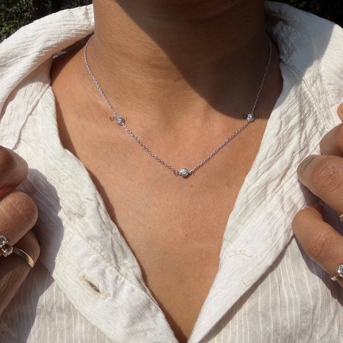 Daylight angle view of white gold three stone bezel set diamond station chain necklace worn on neck