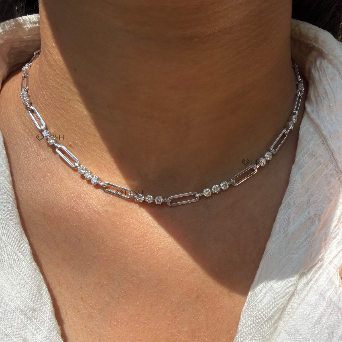 Daylight macro view of white gold round diamond stations alternating with paperclip links worn on neck