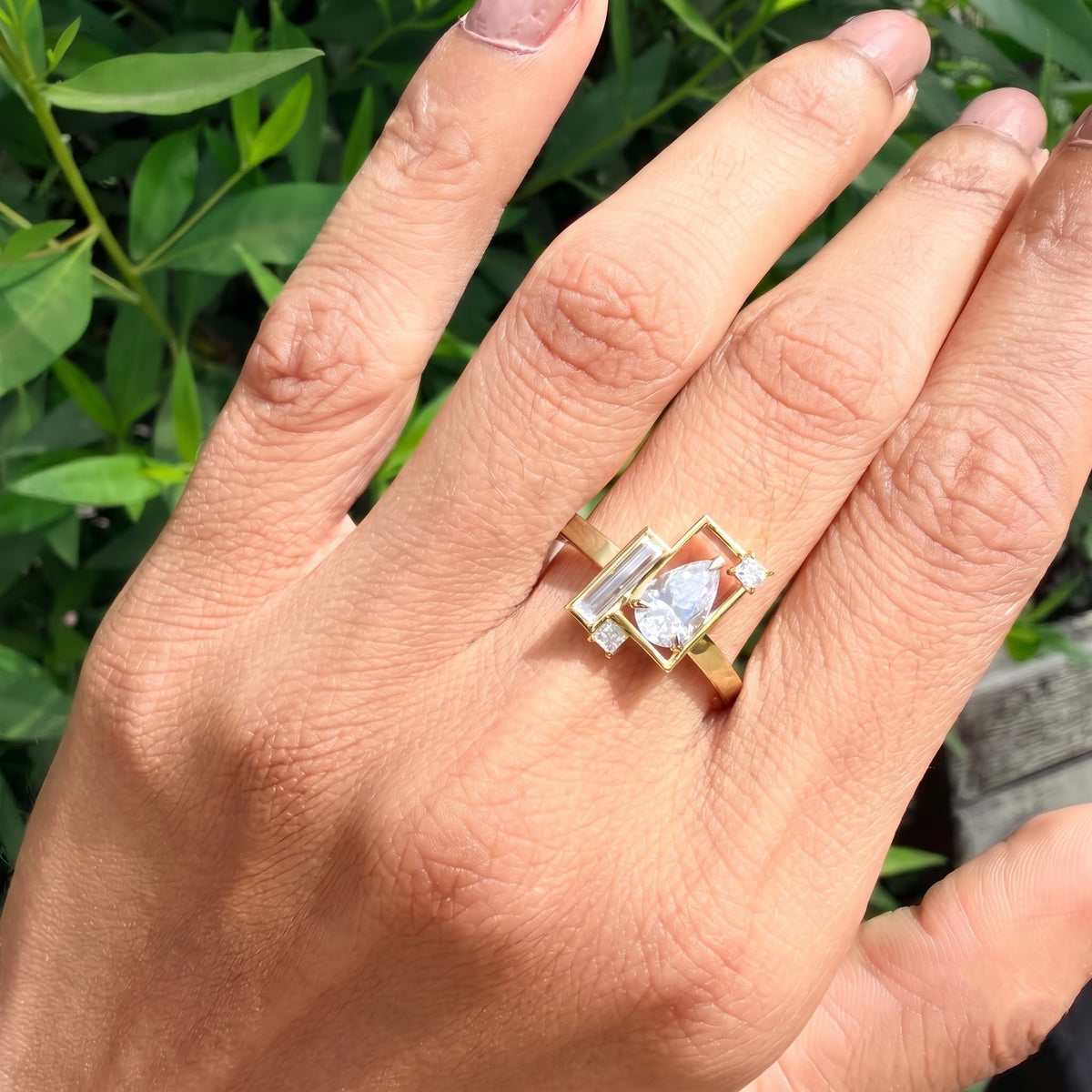 Yellow gold modern geometric mixed-cut diamond ring styled on hand against natural foliage