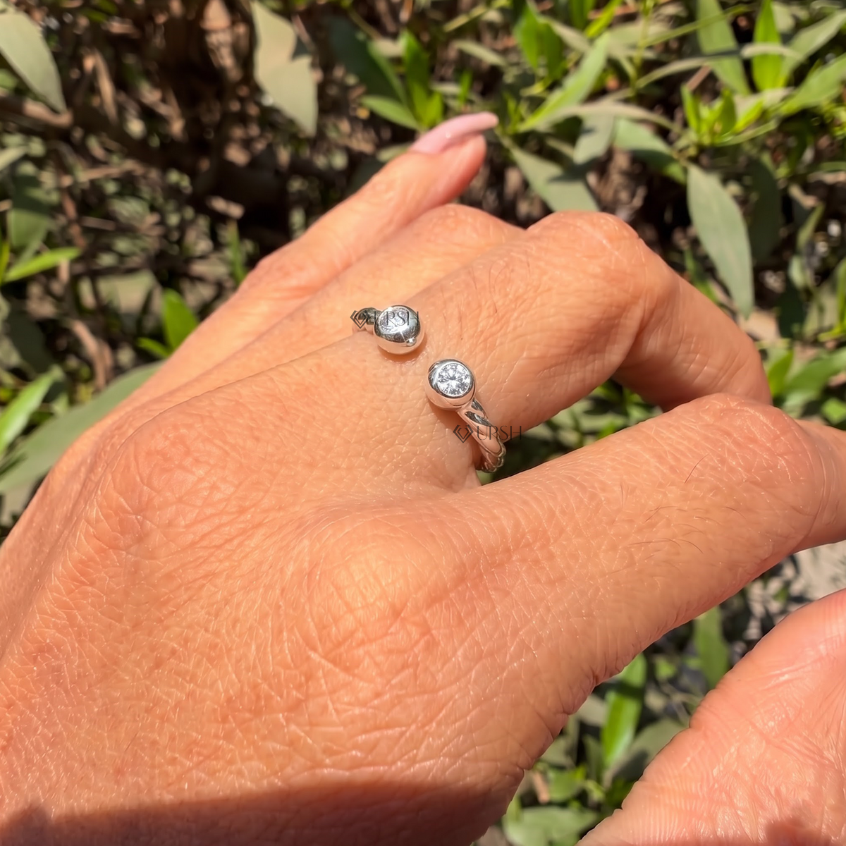 Detailed daylight macro close-up of bezel-set round lab diamonds on open twisted band worn on hand