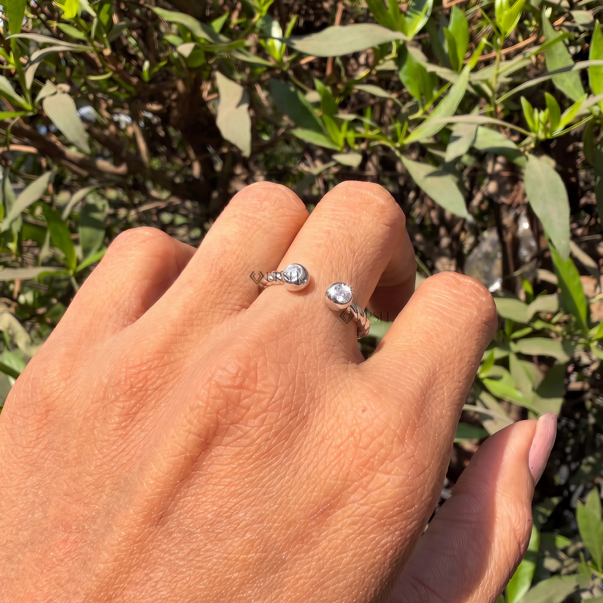Close-up view of bezel-set round brilliant lab-grown diamonds on a textured twisted open bypass ring worn on finger in natural daylight