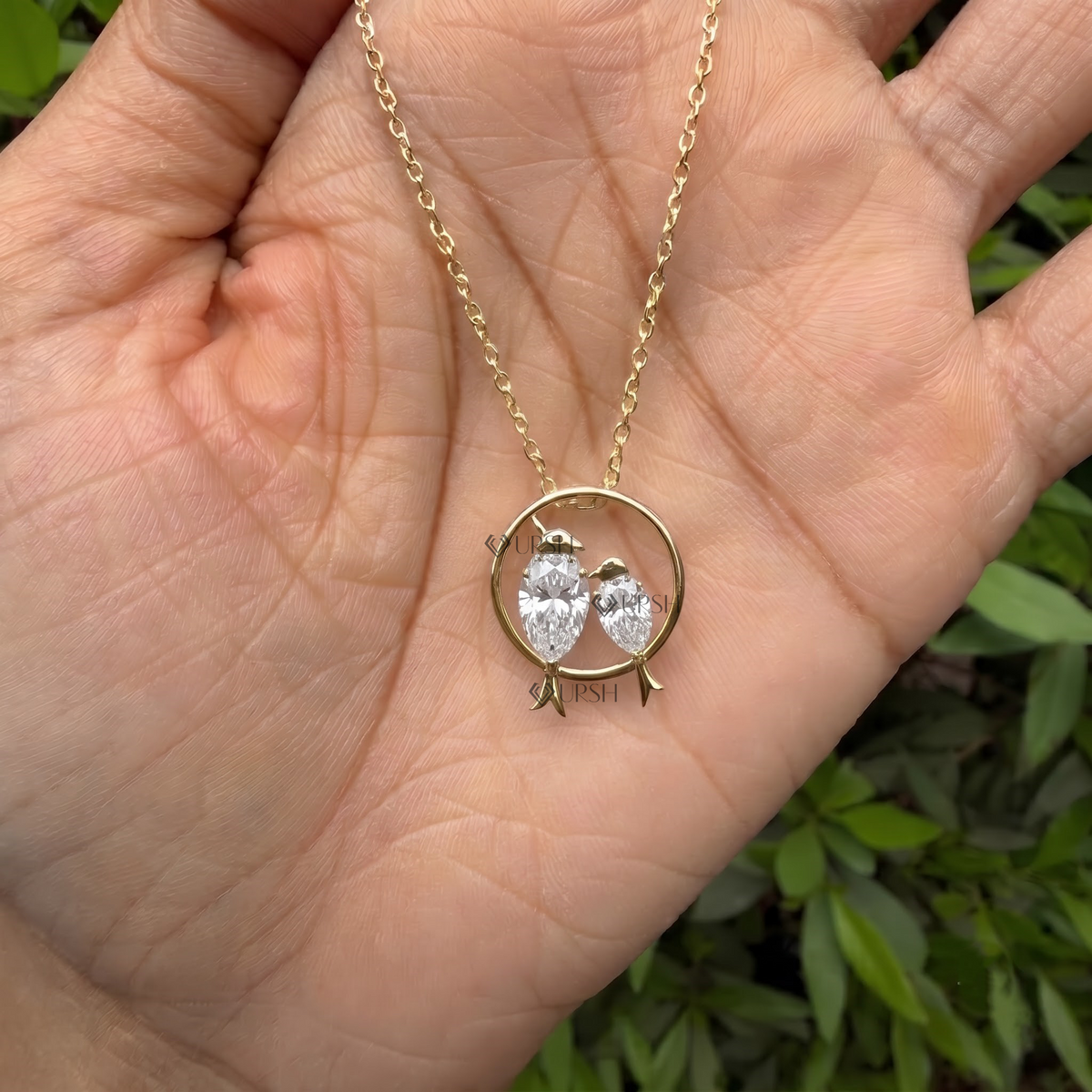 Detailed hand model view of solid yellow gold love birds diamond pendant held between fingers