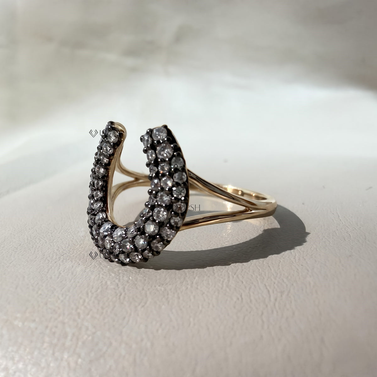 Studio perspective of two-tone horseshoe ring showcasing polished gold split shoulders and textured diamond head