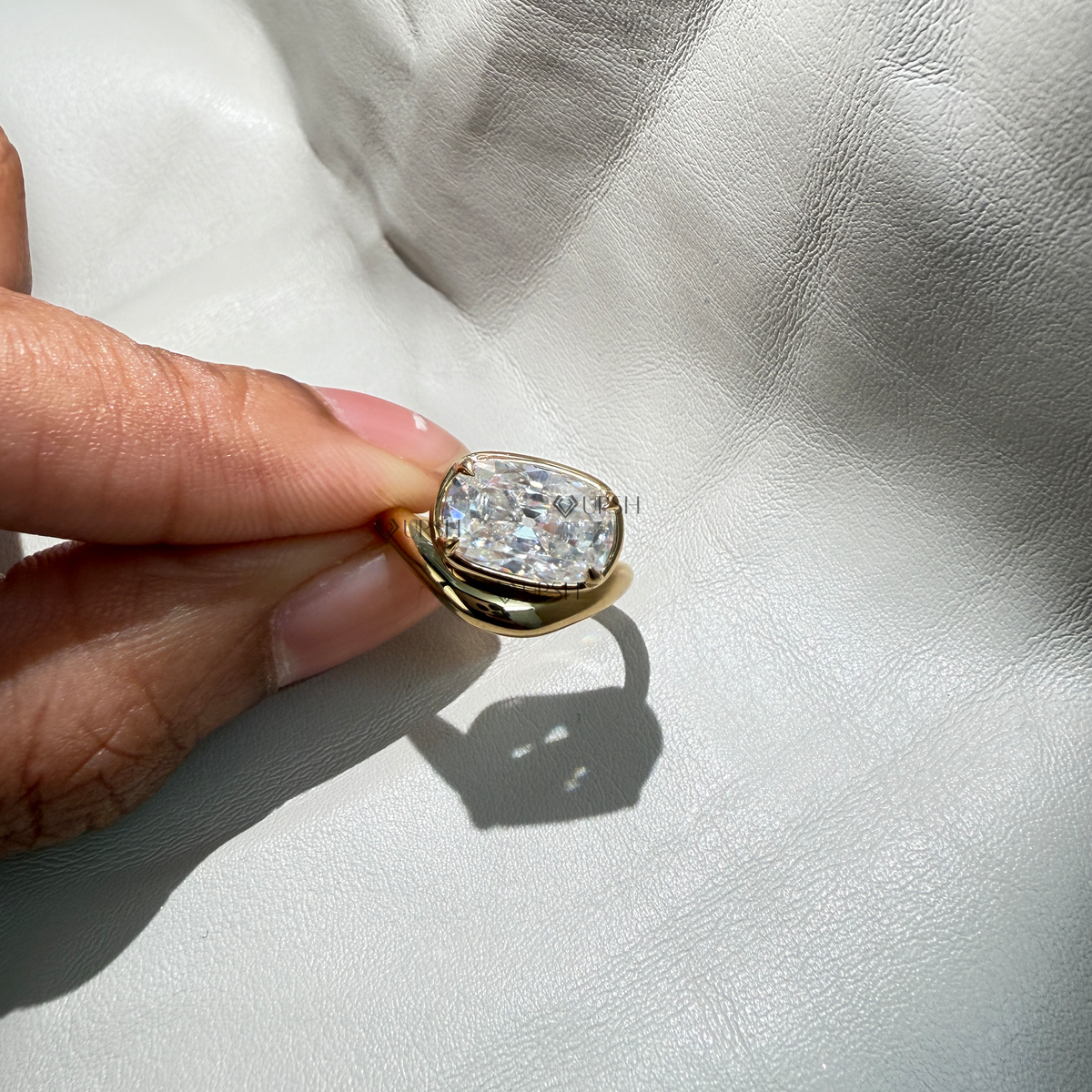 Detailed daylight macro close-up of bezel-set cushion cut lab diamond on wavy crossover band worn on finger