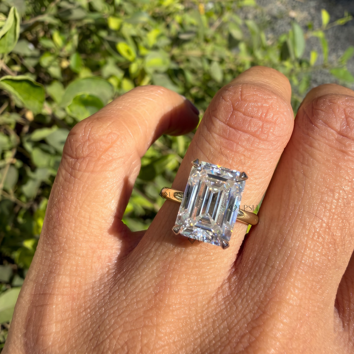 Large emerald cut diamond solitaire catching sunlight on ring finger