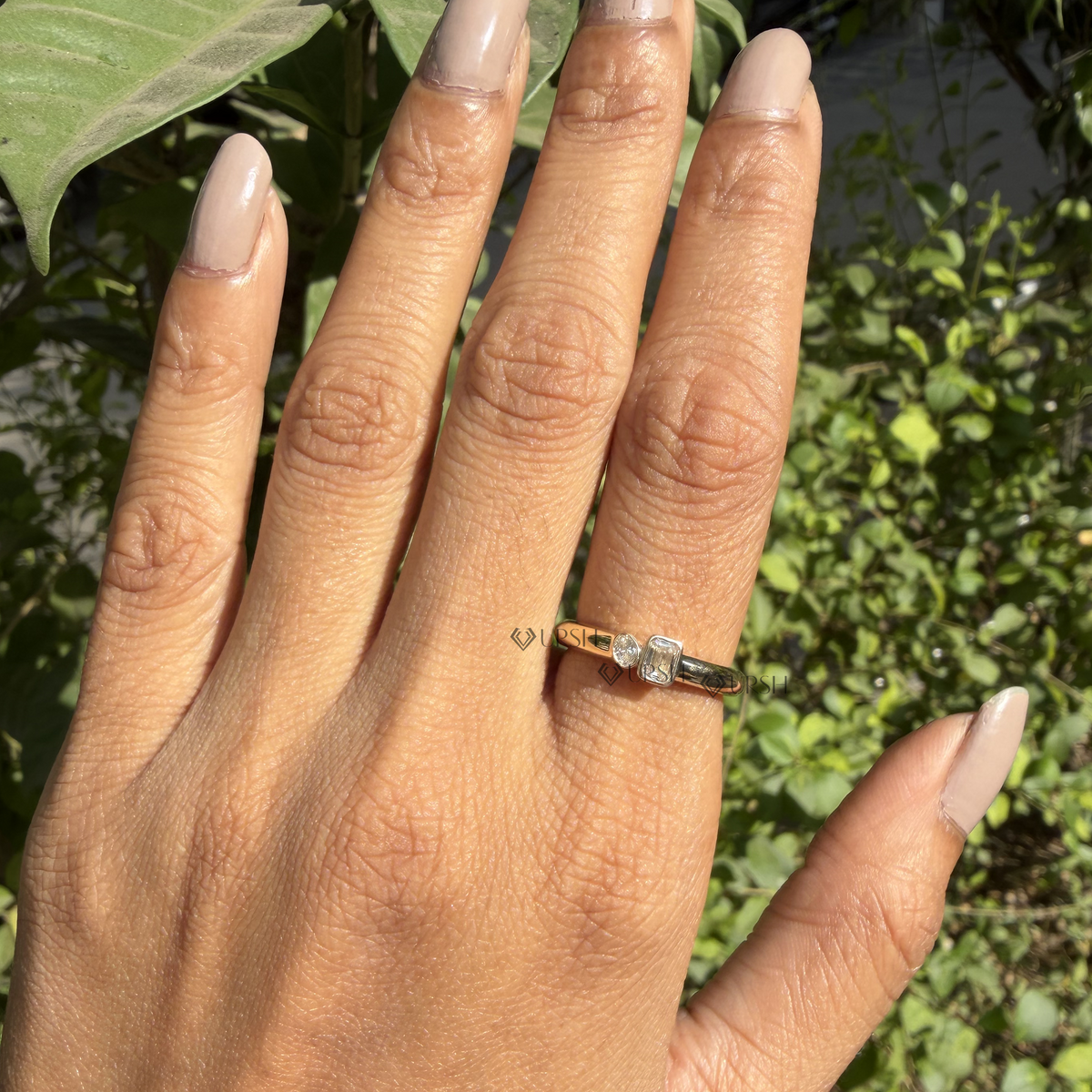 Wide daylight perspective of asymmetric toi et moi ring worn against garden foliage