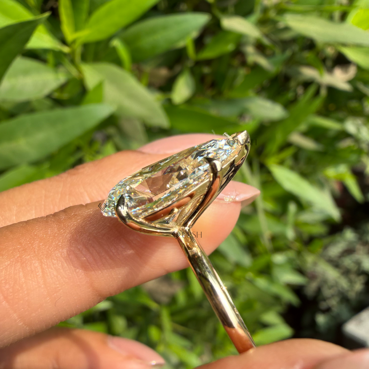 Detailed side-profile daylight view of oversized pear-cut solitaire diamond held against natural garden background