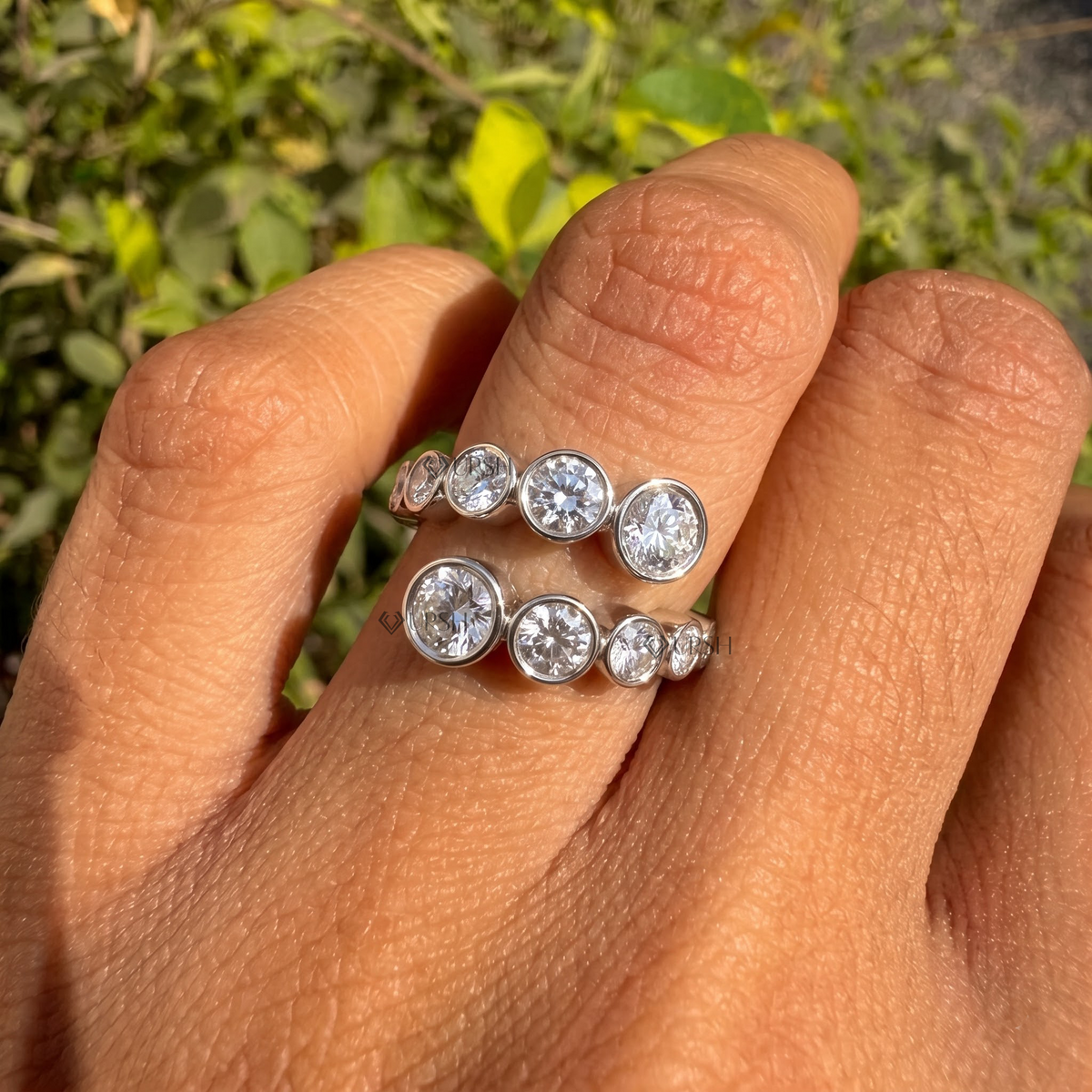 White gold graduated round diamond bypass wrap ring worn against natural garden greenery