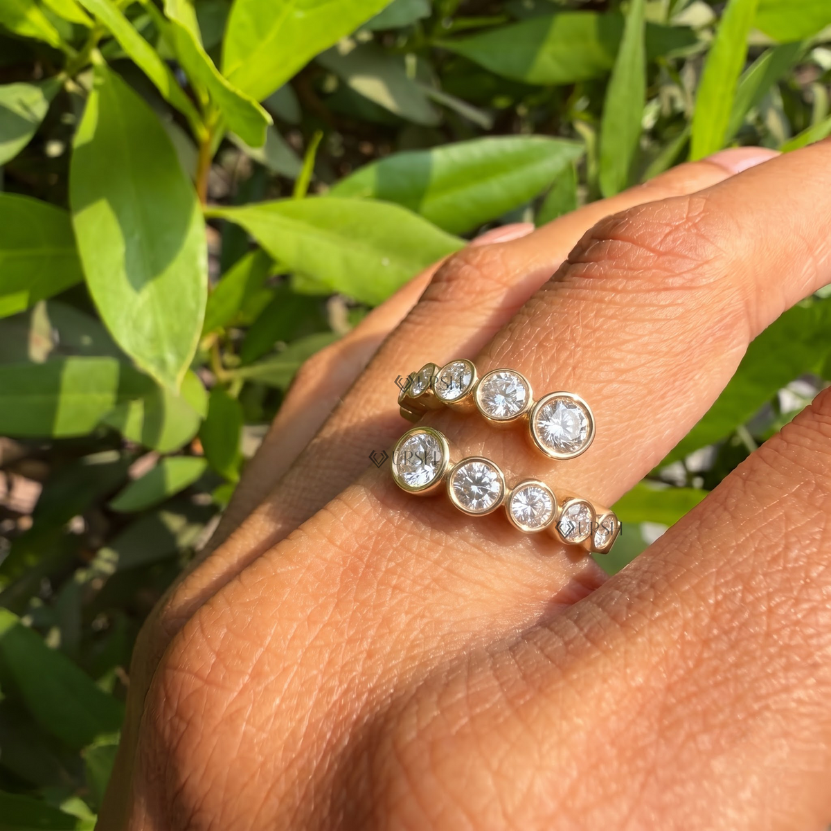Yellow gold bezel-set bypass ring worn on finger against natural foliage