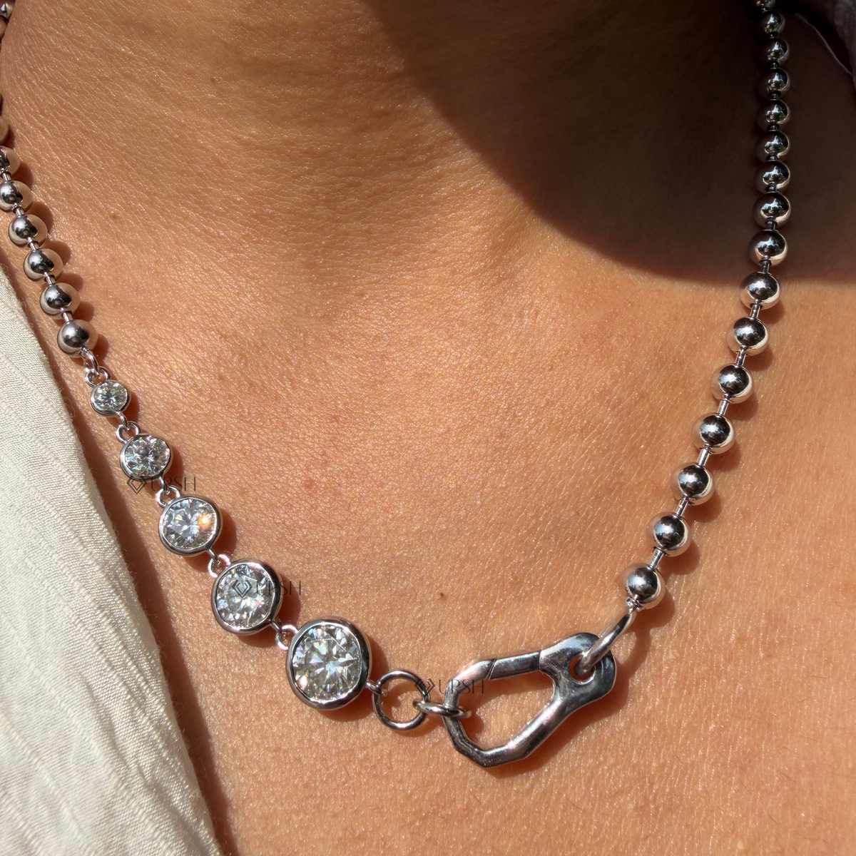 Daylight macro view of white gold graduated bezel set diamonds and carabiner lock on ball chain worn on neck