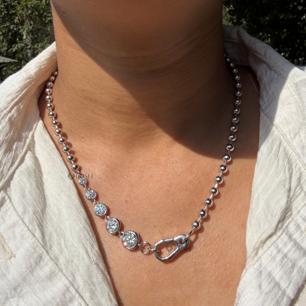 Daylight perspective of white gold graduated bezel diamond ball bead chain worn against collarbone