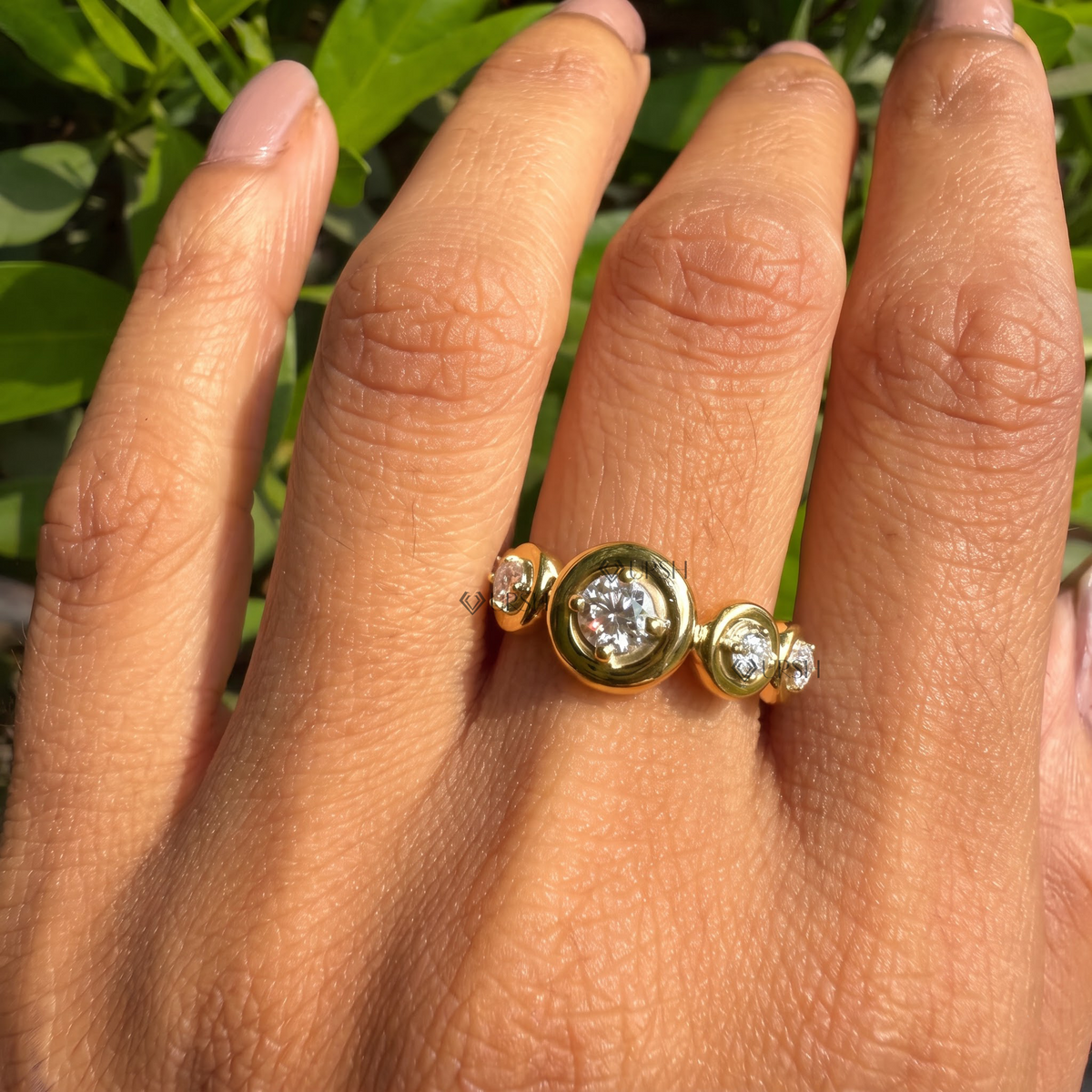 Yellow gold bezel-set station ring worn on finger against natural foliage.