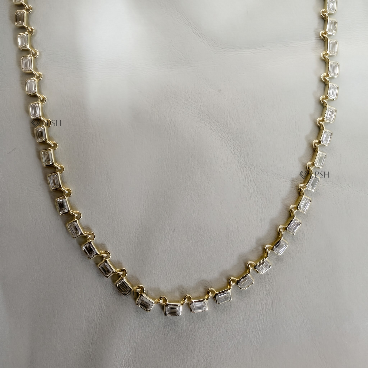 Solid gold tennis style necklace featuring Emerald cut lab grown diamonds set horizontally in alternating linked bezels resting flat on neutral background