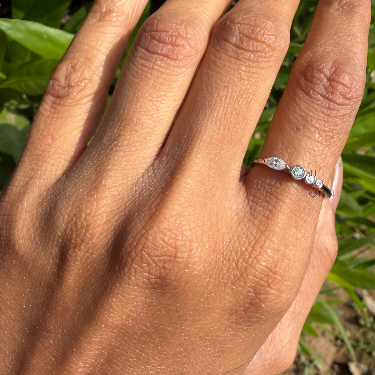 Wide daylight perspective of asymmetric cluster ring worn against natural garden foliage