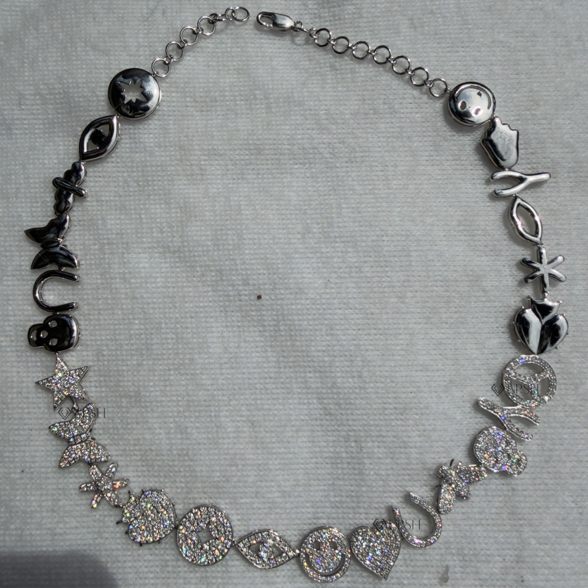 Solid white gold multi-charm eclectic diamond station chain resting flat on neutral surface