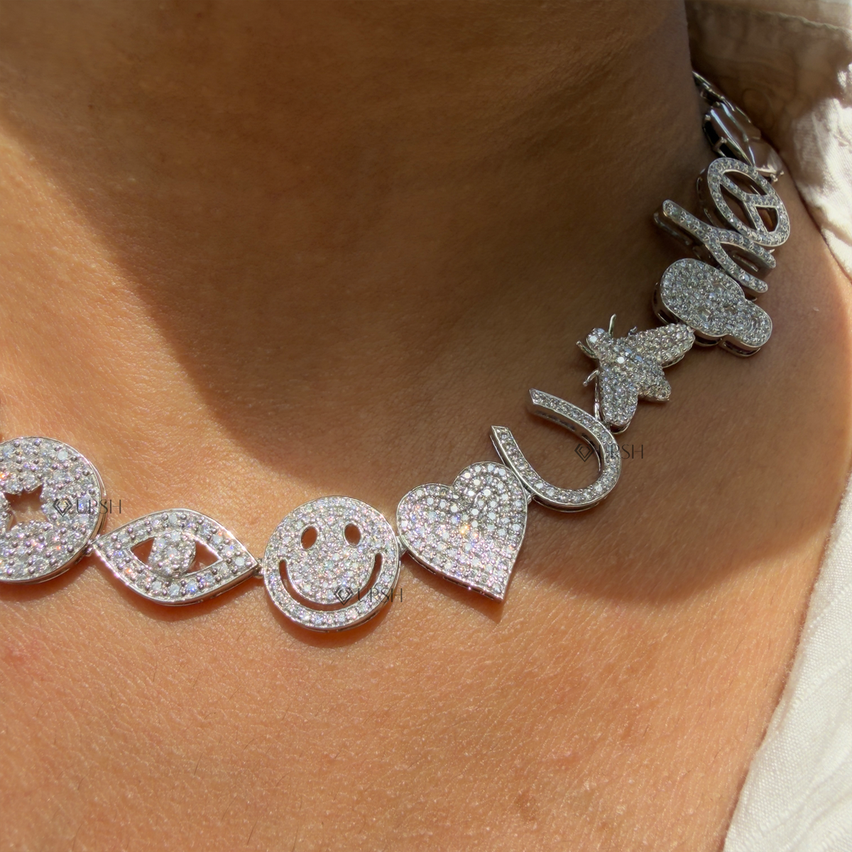 Daylight macro view of white gold multi-charm diamond station collar necklace detailing smiley, evil eye, heart, and bee motifs
