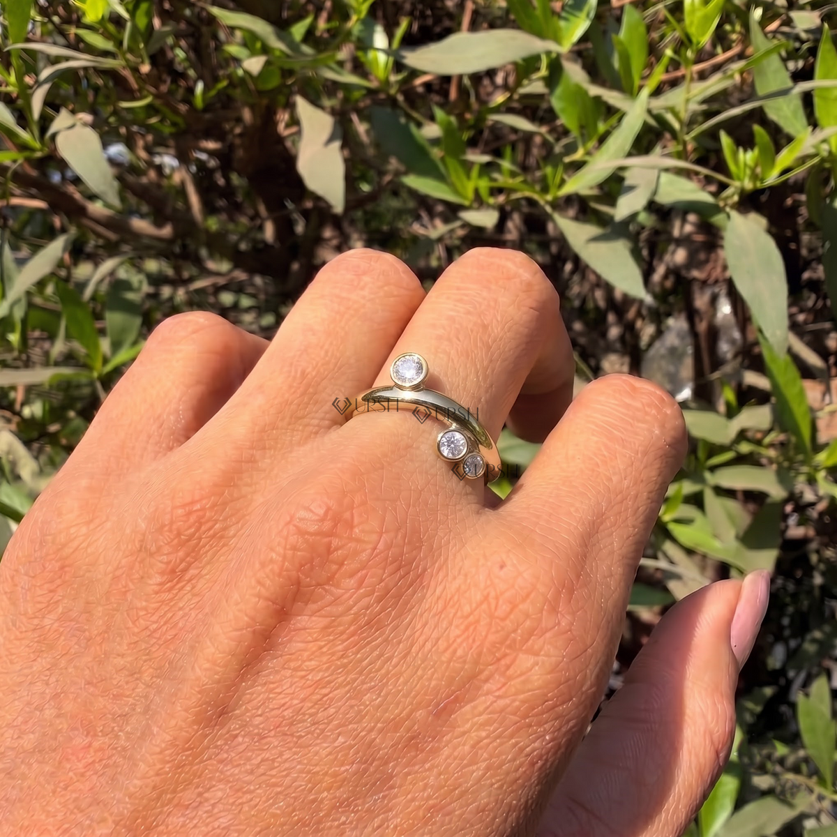 Daylight perspective of curved scattered diamond ring worn against natural garden background