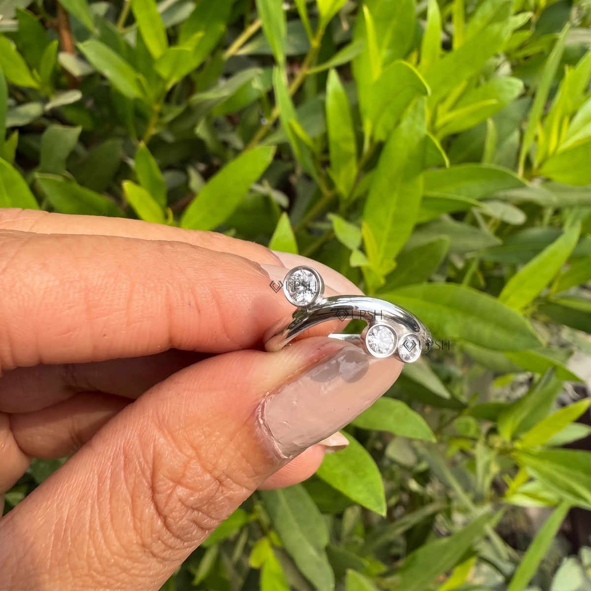 Detailed daylight macro close-up of bezel-set scattered round diamond cluster on curved band worn on finger