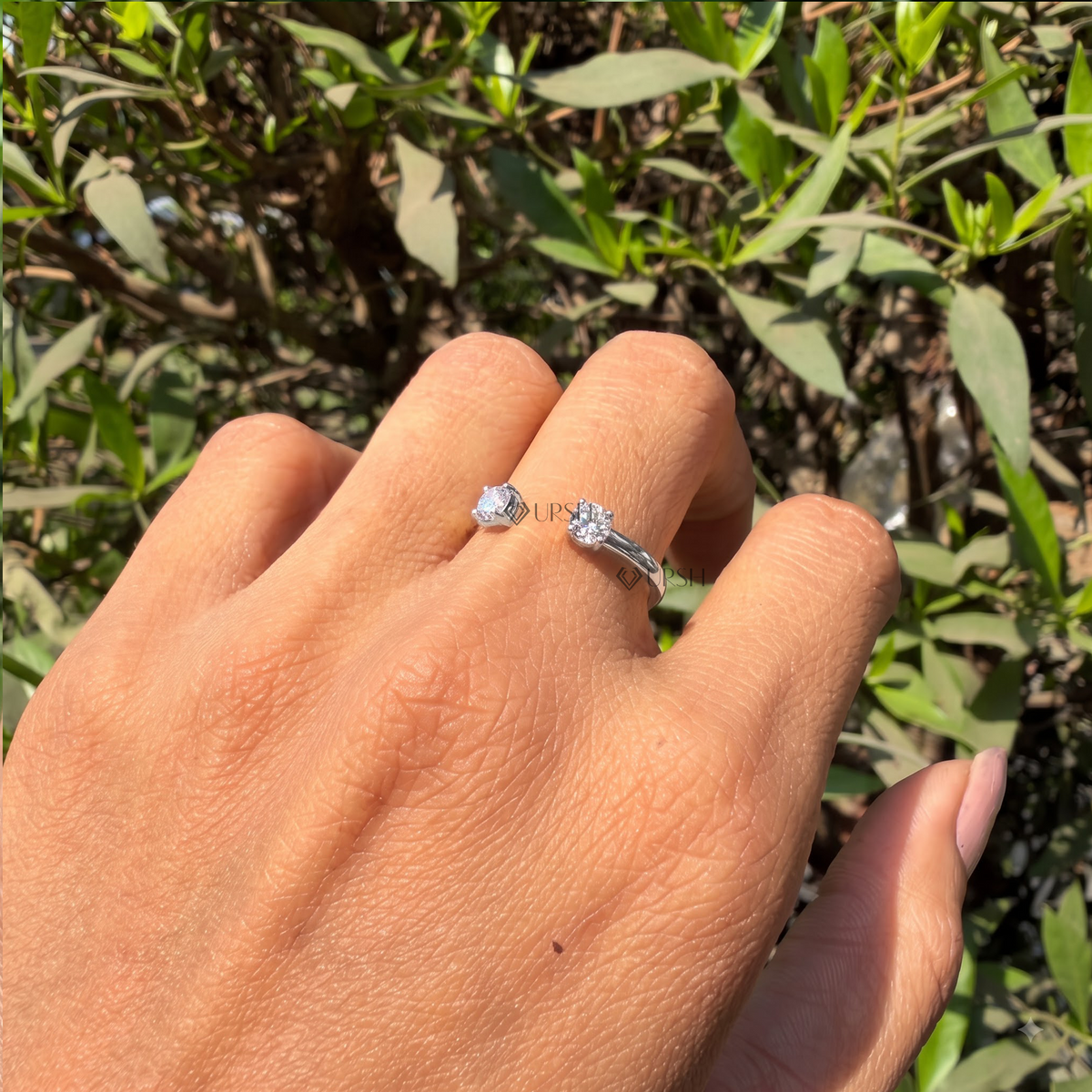 Open cuff diamond stacking band catching sunlight on ring finger against green leaves