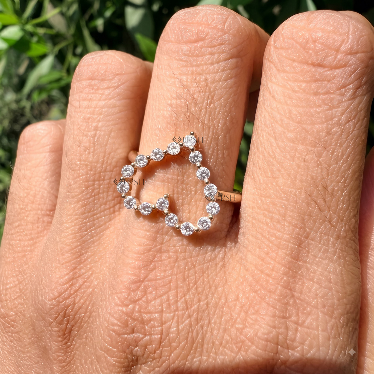 Romantic openwork diamond heart ring catching sunlight on hand against lush greenery