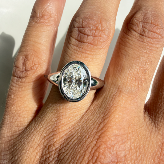 Oval bezel solitaire engagement ring styled gracefully on finger in natural daylight