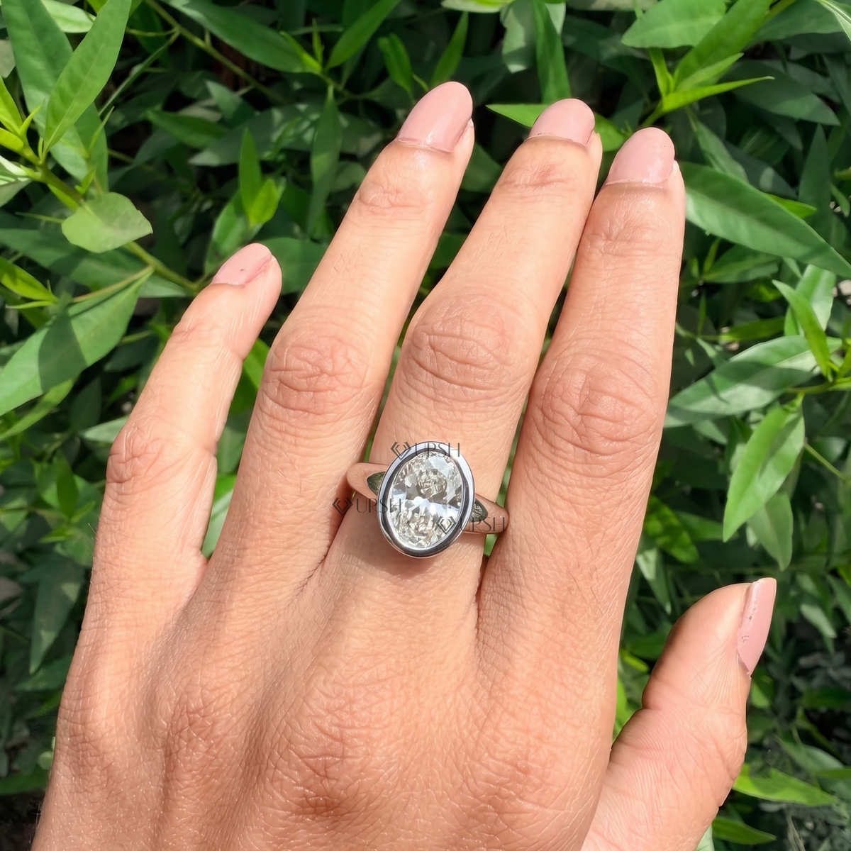 Detailed daylight close-up of oval brilliant lab-grown diamond in seamless bezel setting worn on hand