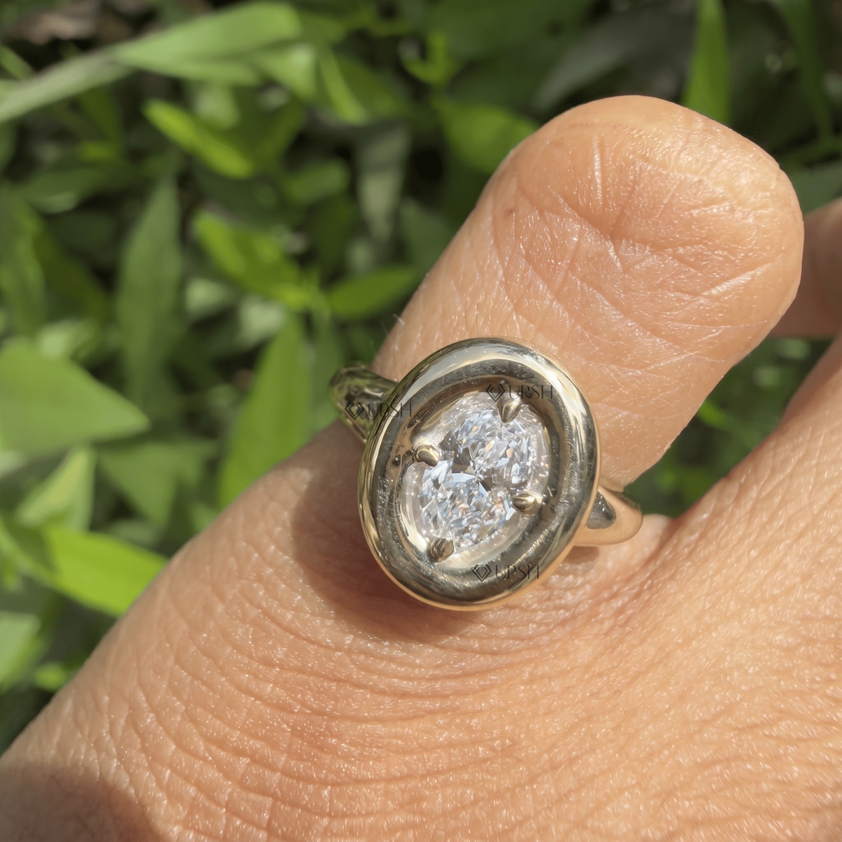 Daylight perspective of oval halo statement ring worn against natural garden background