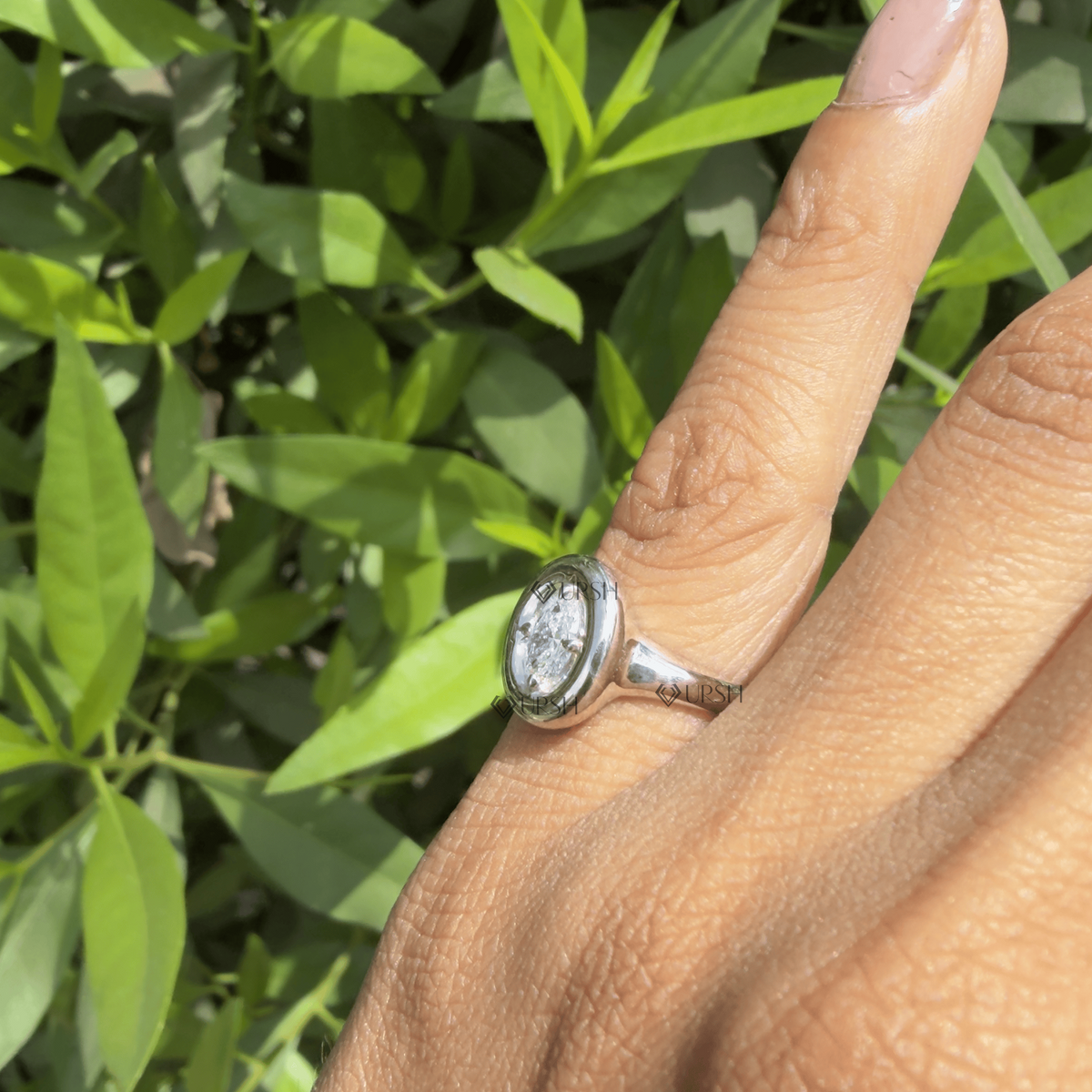 Side profile view of oval bezel statement ring held against natural outdoor background