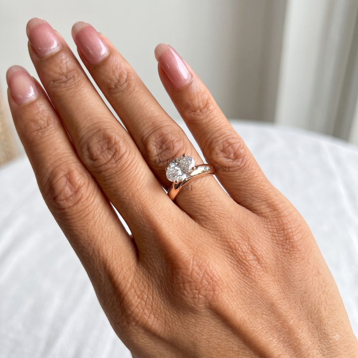 A close-up of a hand wearing a rose gold ring with a heart-shaped diamond cluster, set against a soft, blurred background.
