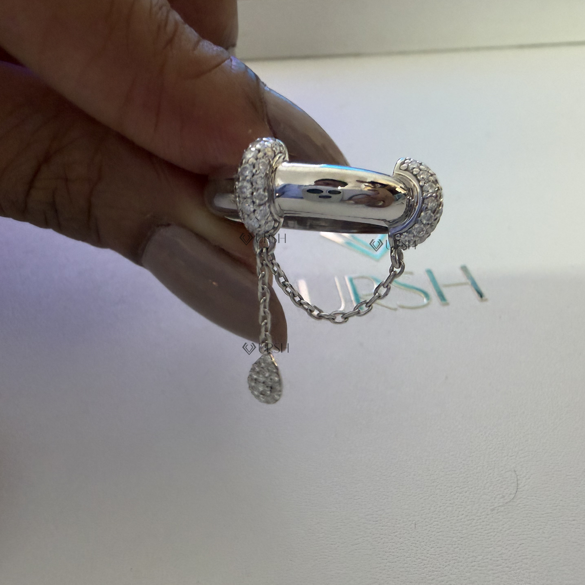Close-up studio view of dangle chain statement ring held against presentation box background