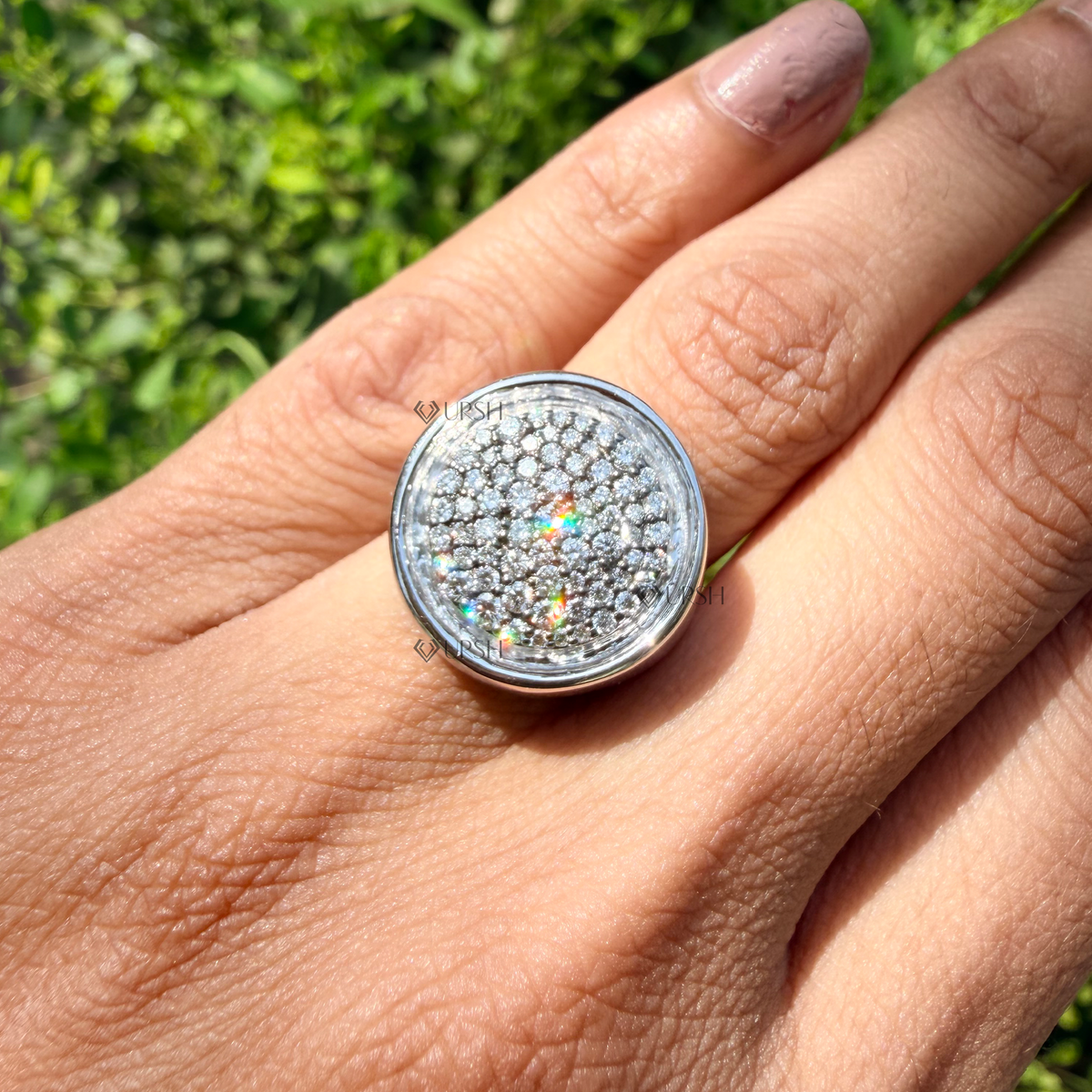 White gold circular pavé signet band worn against natural garden greenery