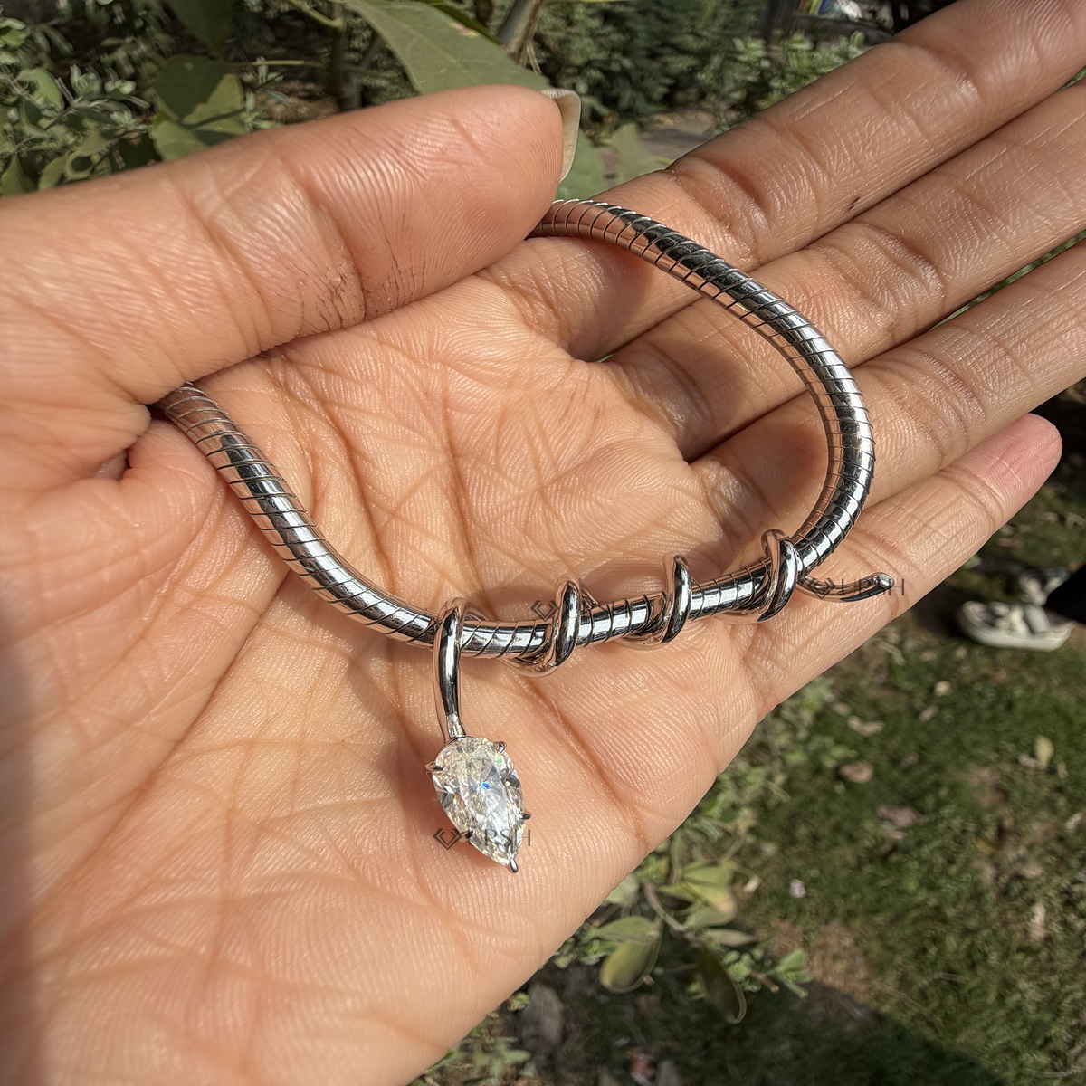 Detailed macro shot of white gold spiral wire charm and suspended pear diamond held gracefully in hand