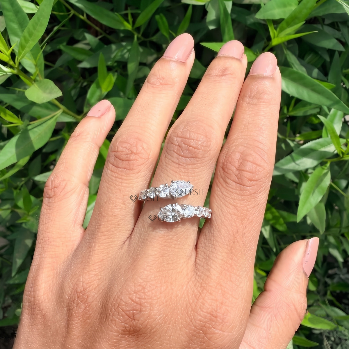 Wide daylight perspective of graduated bypass diamond ring worn against natural garden foliage