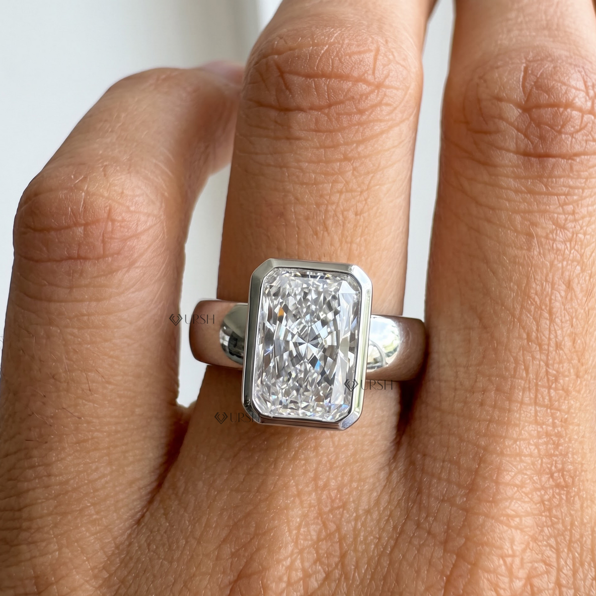 Front perspective close up of white gold radiant diamond bezel ring on finger