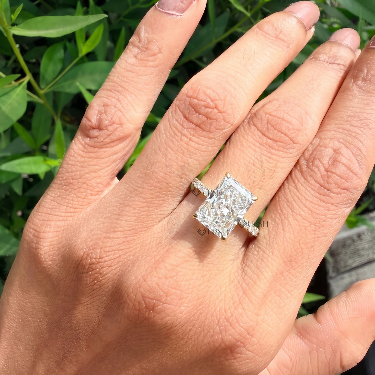 White gold radiant cut engagement ring worn against natural garden greenery