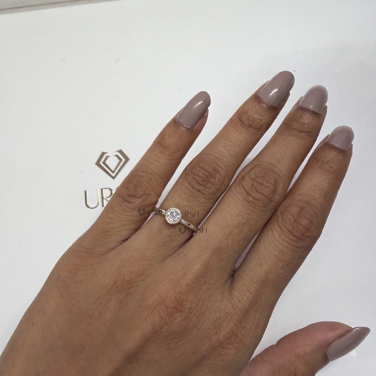White gold dainty round bezel engagement ring styled on ring finger against clean studio backdrop