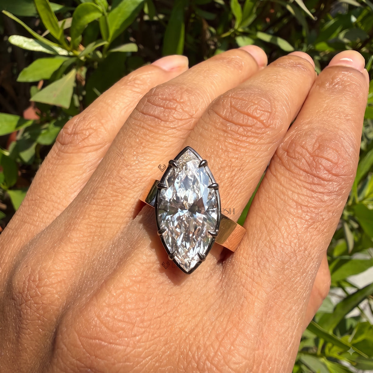 Wide rose gold cigar band marquise ring styled on finger against natural garden greenery