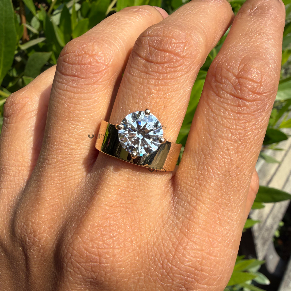 Wide gold cigar band solitaire ring styled on finger against natural garden greenery