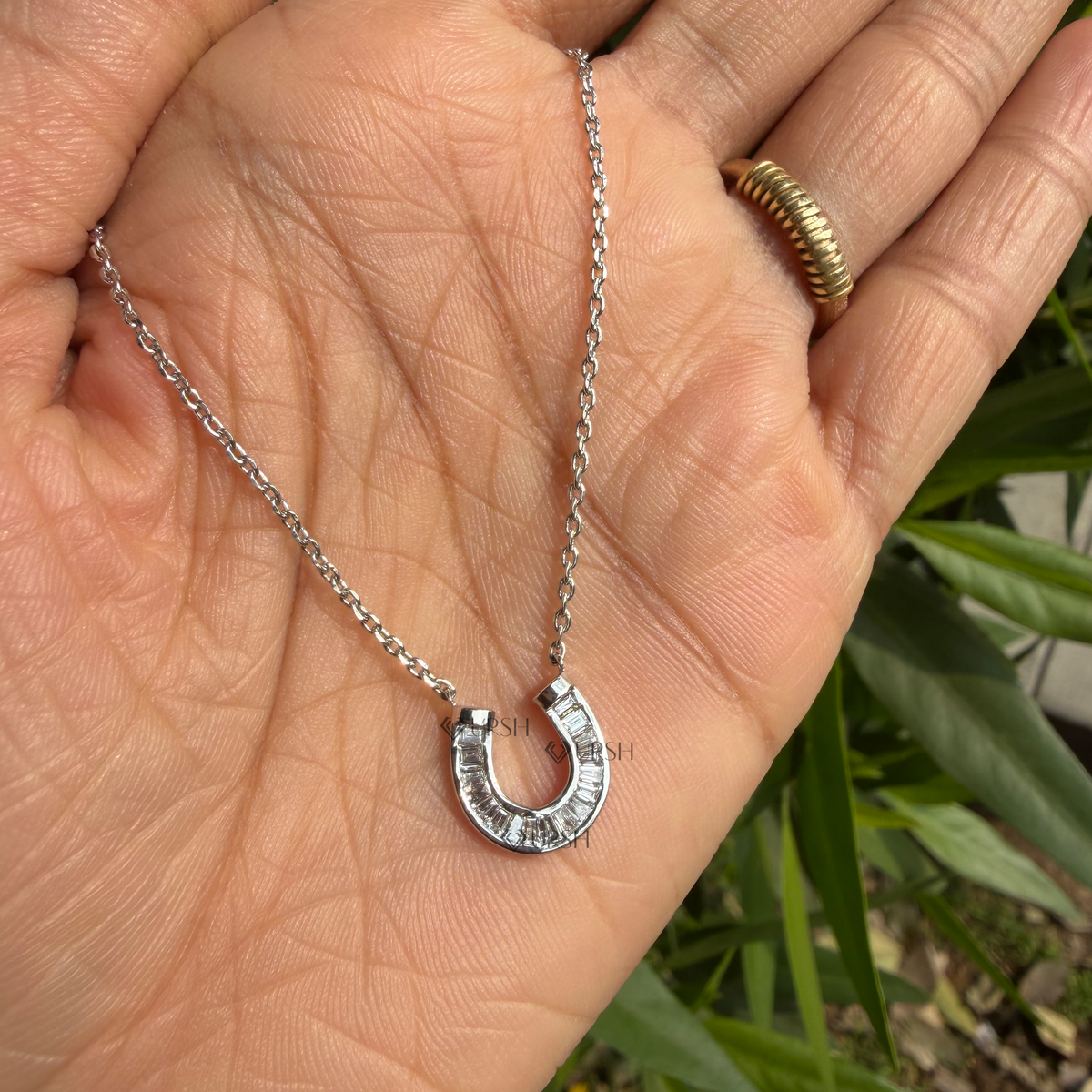 Detailed hand model view of solid white gold baguette diamond horseshoe pendant held gracefully