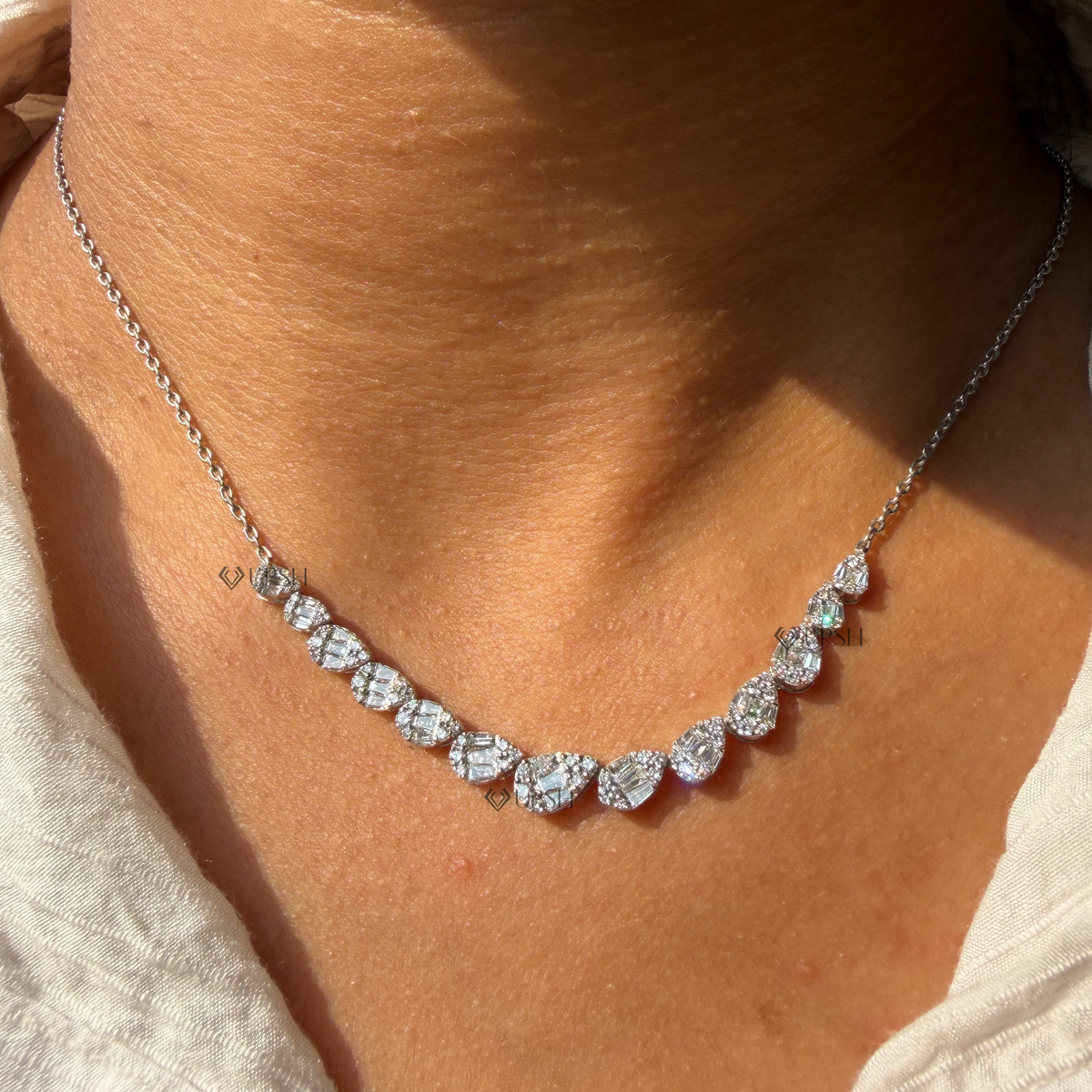 Daylight angle view of white gold mosaic pear cluster diamond station necklace resting on collarbone