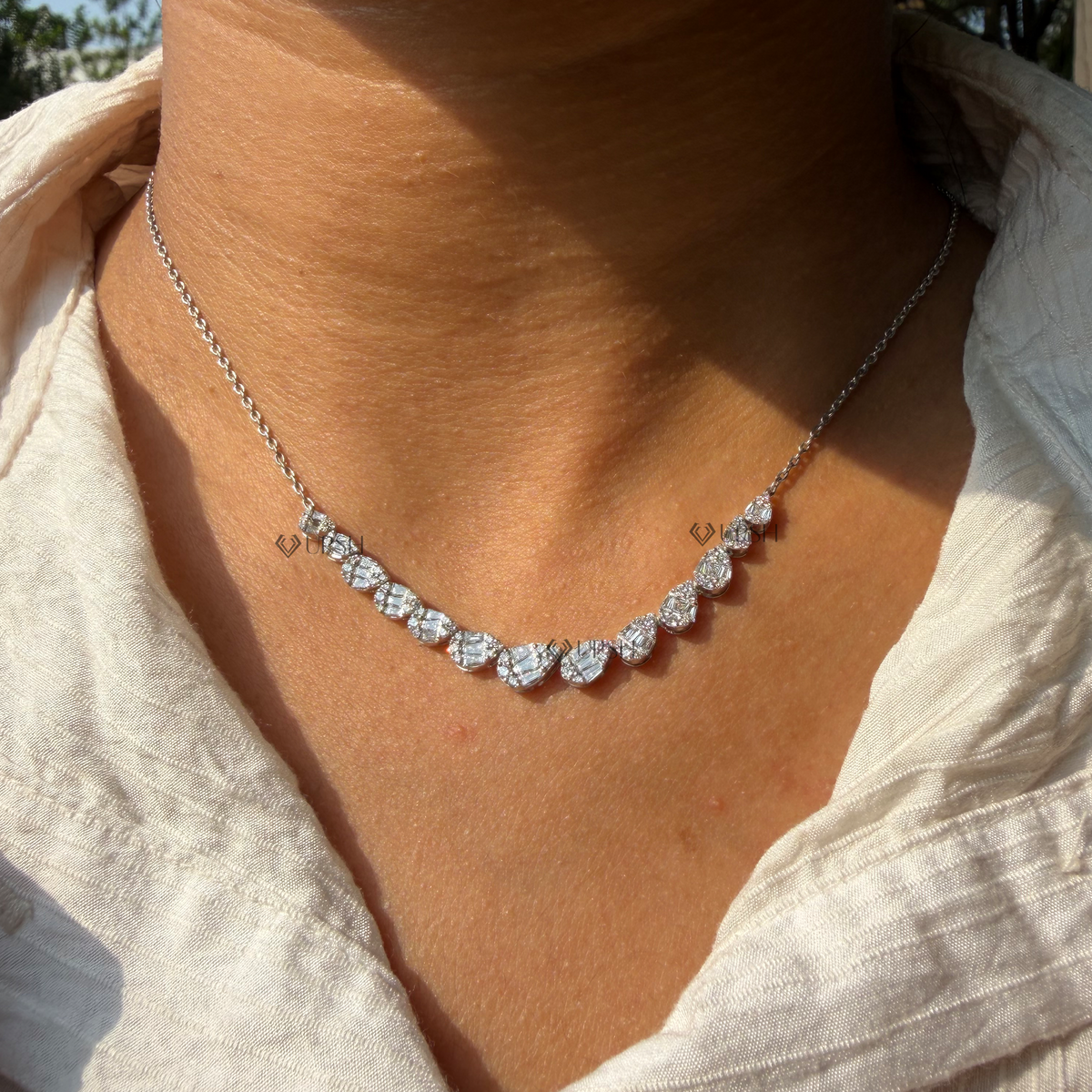 Daylight macro view of white gold graduated pear cluster diamond station necklace worn on neck