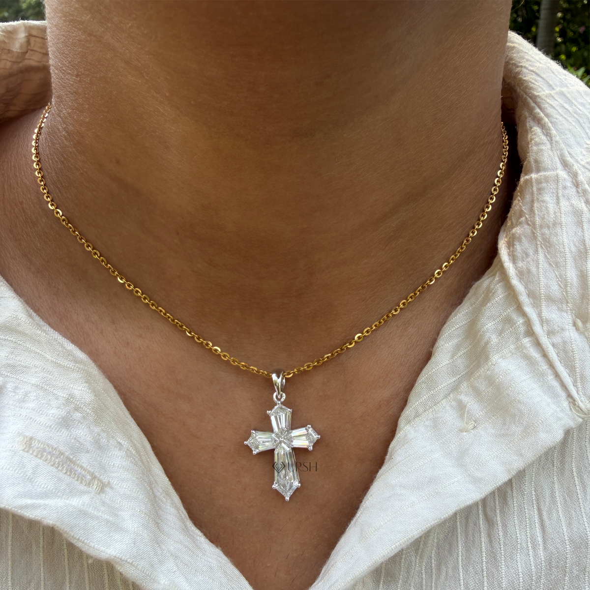 A close-up of a person's neck and upper chest wearing a delicate gold chain necklace with a silver-toned cross pendant featuring a clear faceted center stone.