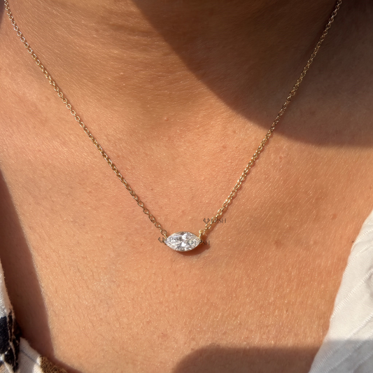 Yellow gold horizontal east-west marquise diamond solitaire pendant necklace styled gracefully on neck in natural daylight
