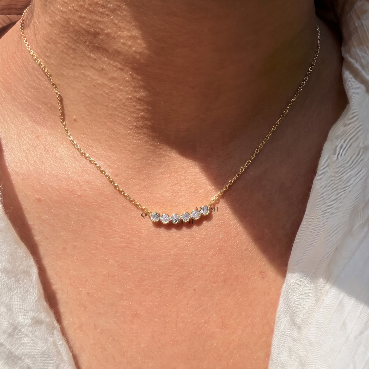 Daylight perspective view of yellow gold curved bezel diamond bar pendant resting along collarbone