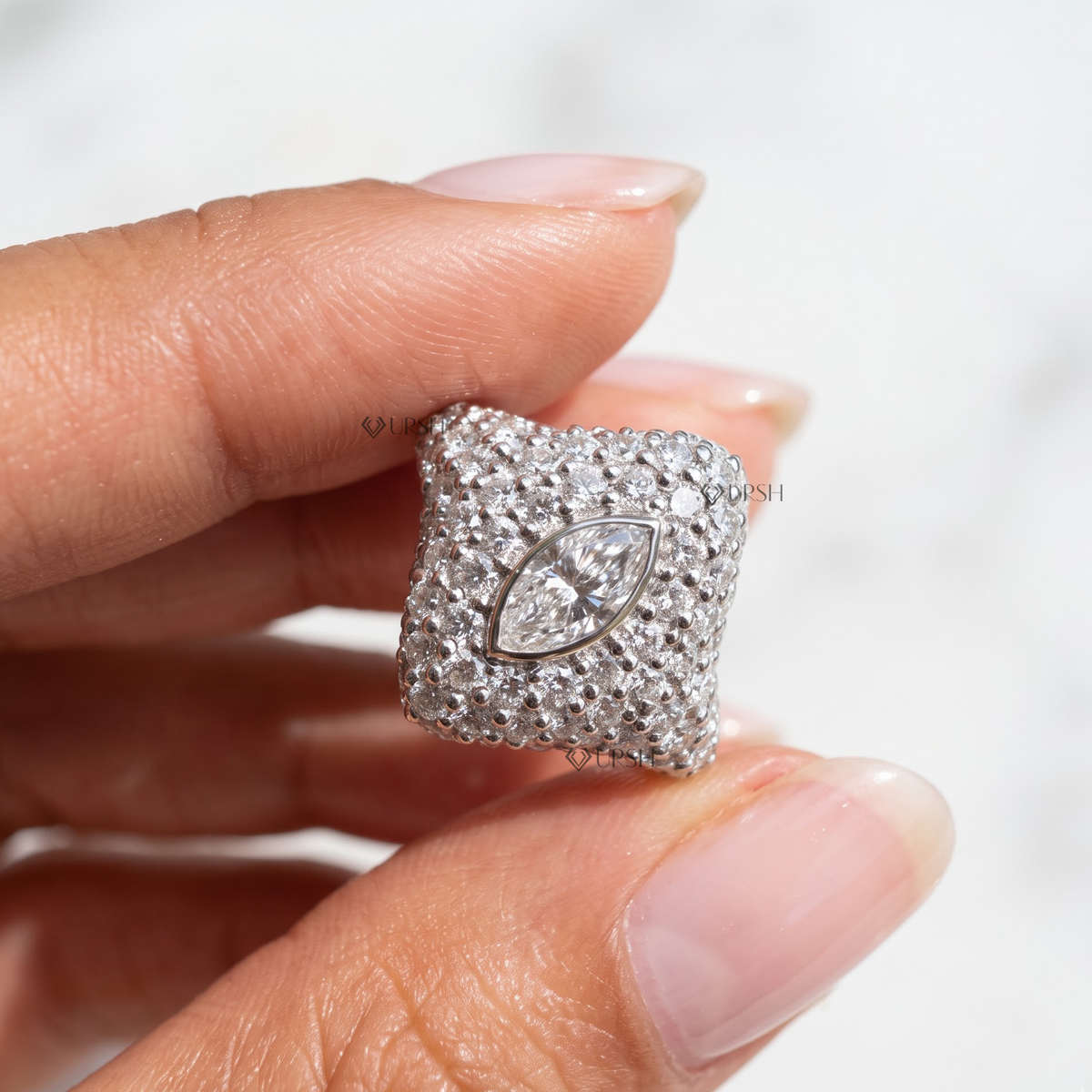 Macro view of white gold marquise diamond pave statement ring held between fingers.