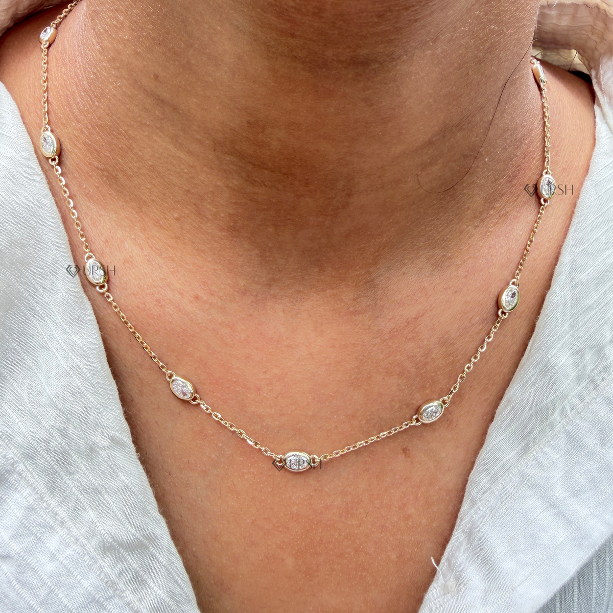 Yellow gold bezel set oval cut diamond station chain necklace styled gracefully on neck in natural daylight