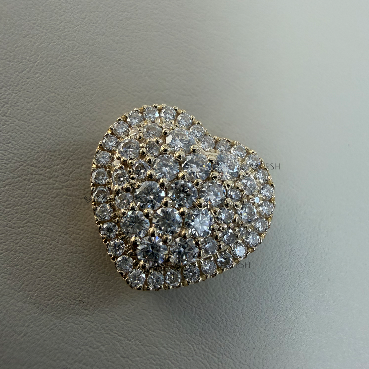 Macro view of yellow gold pavé diamond heart pendant resting flat on neutral surface