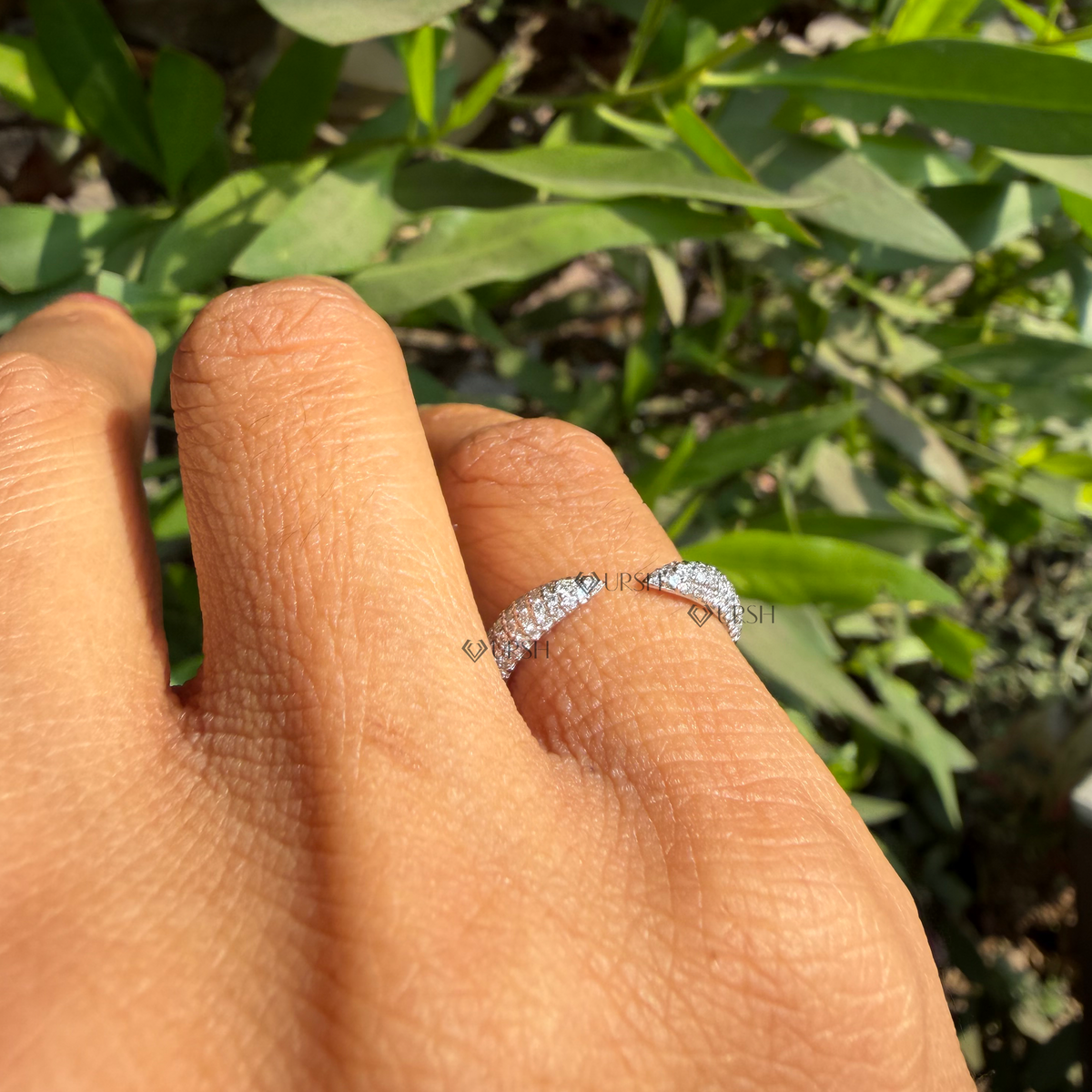 Daylight perspective of pavé diamond bypass ring worn against natural garden background