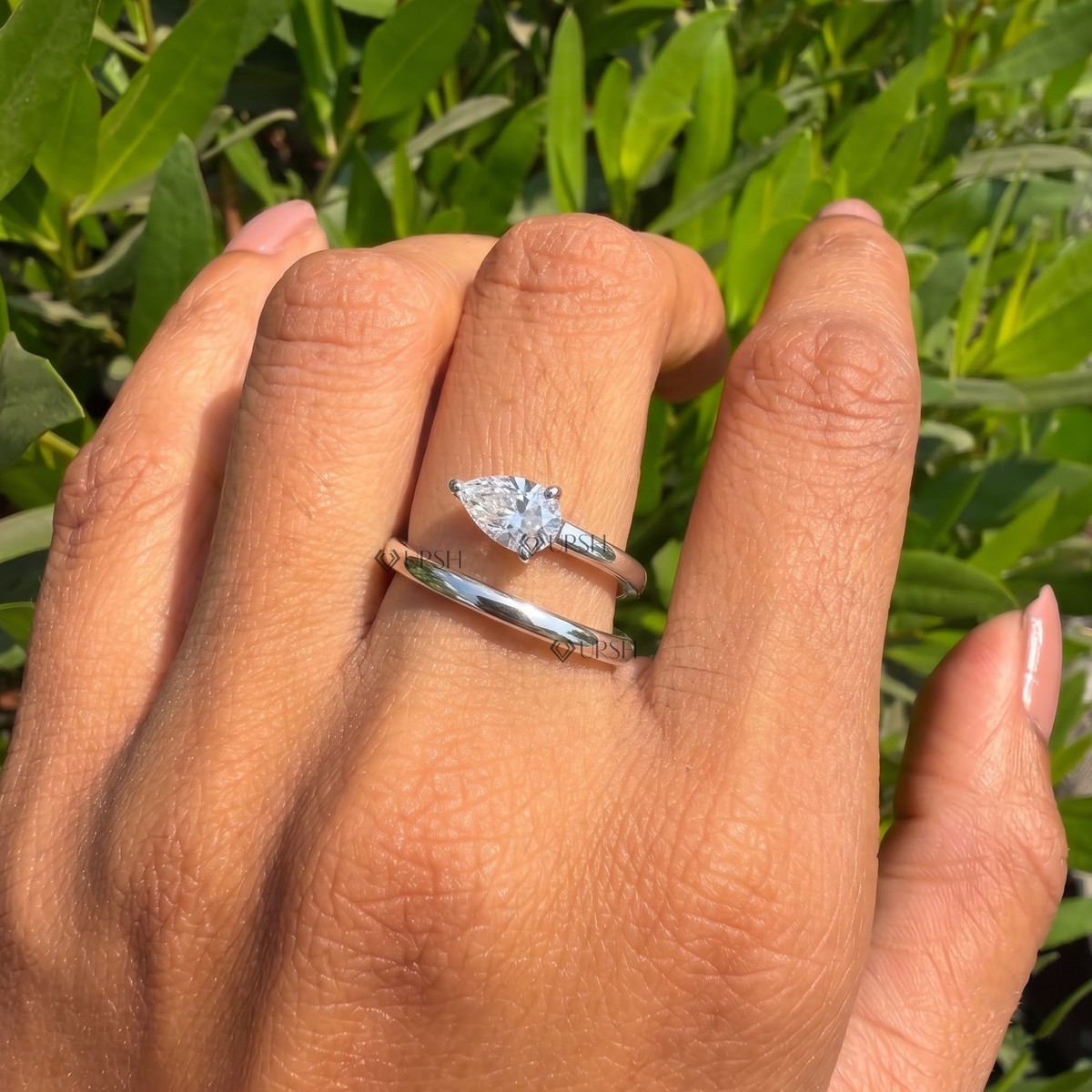 Pear-cut diamond spiral bypass ring styled gracefully on finger in natural daylight