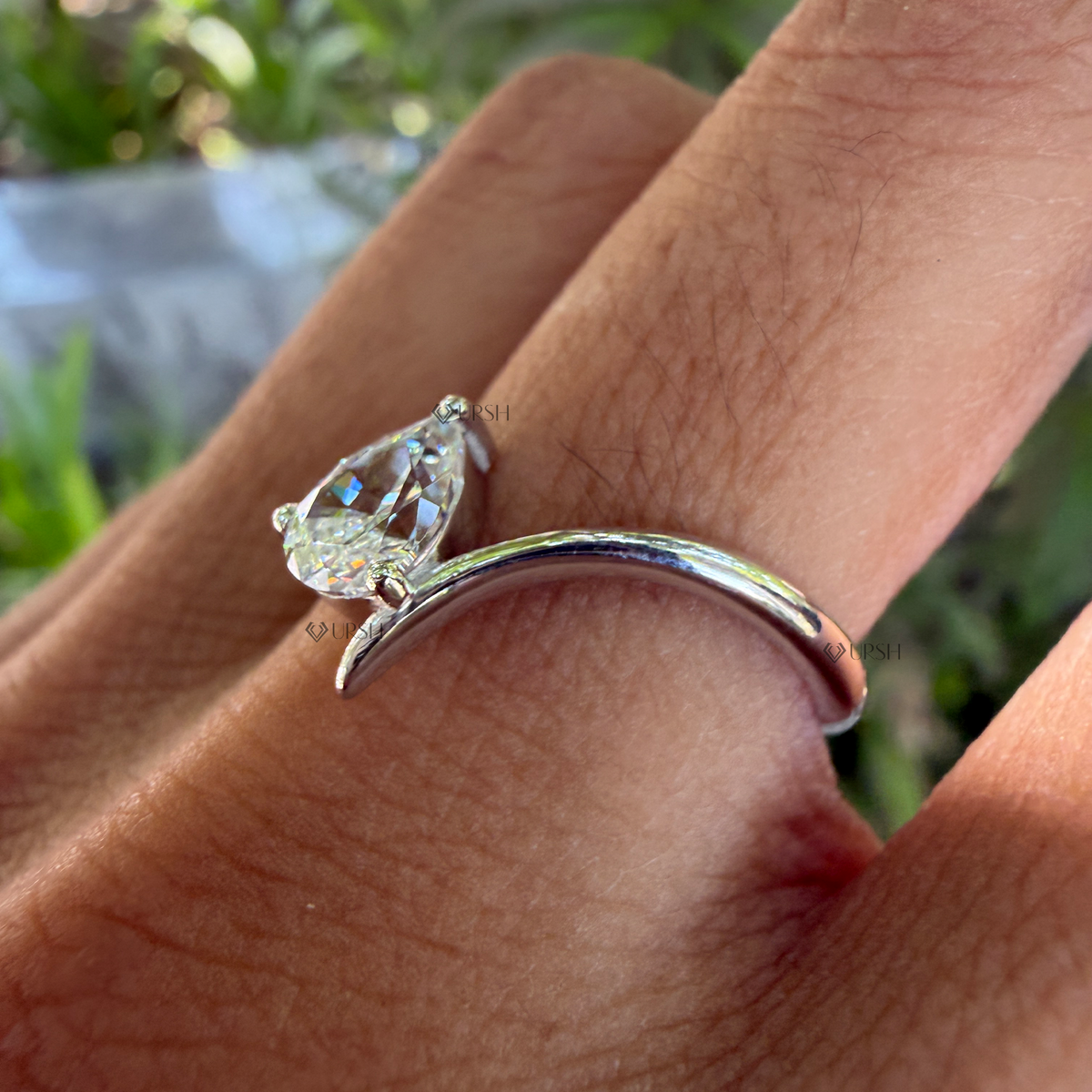 Side angle showing fluid bypass curve and raised prong setting of pear diamond ring on hand